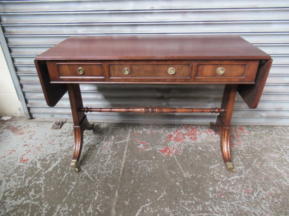 A mahogany sofa table featuring drop-leaf sides, front drawers with brass ring handles, a turned stretcher, and splayed sabre legs with brass castors. View II