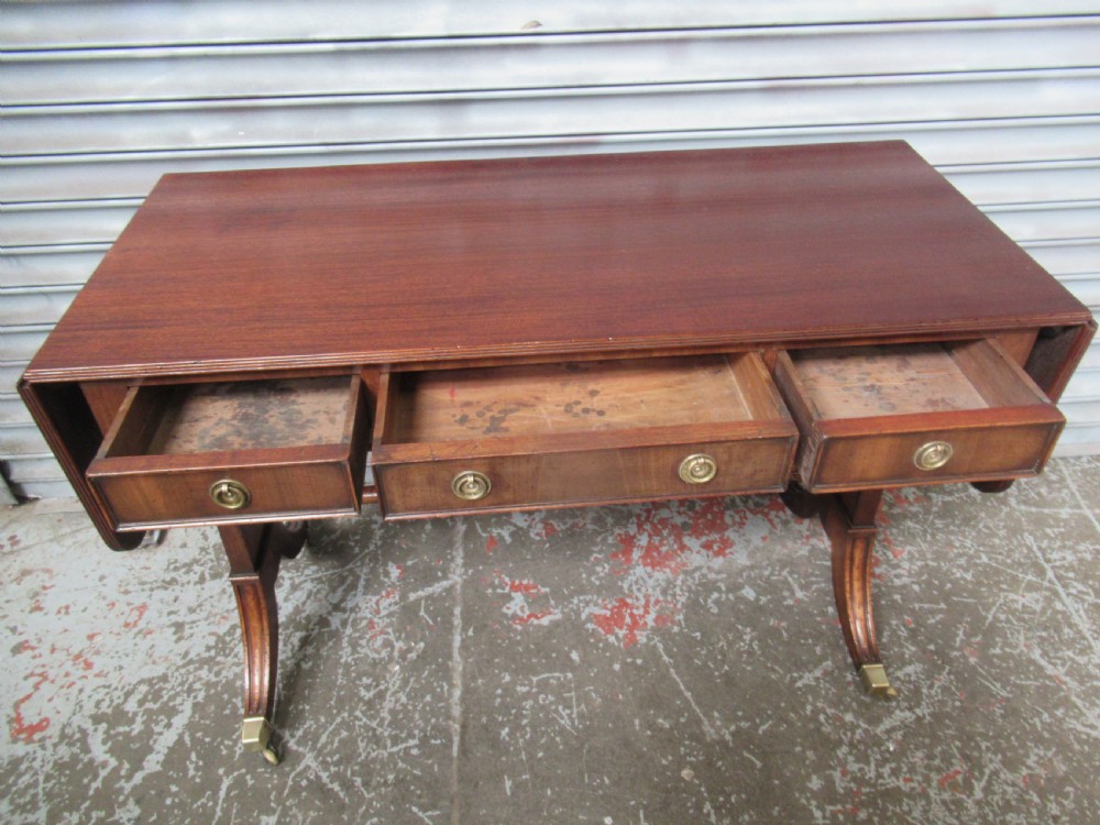 A mahogany sofa table featuring drop-leaf sides, front drawers with brass ring handles, a turned stretcher, and splayed sabre legs with brass castors. View VI