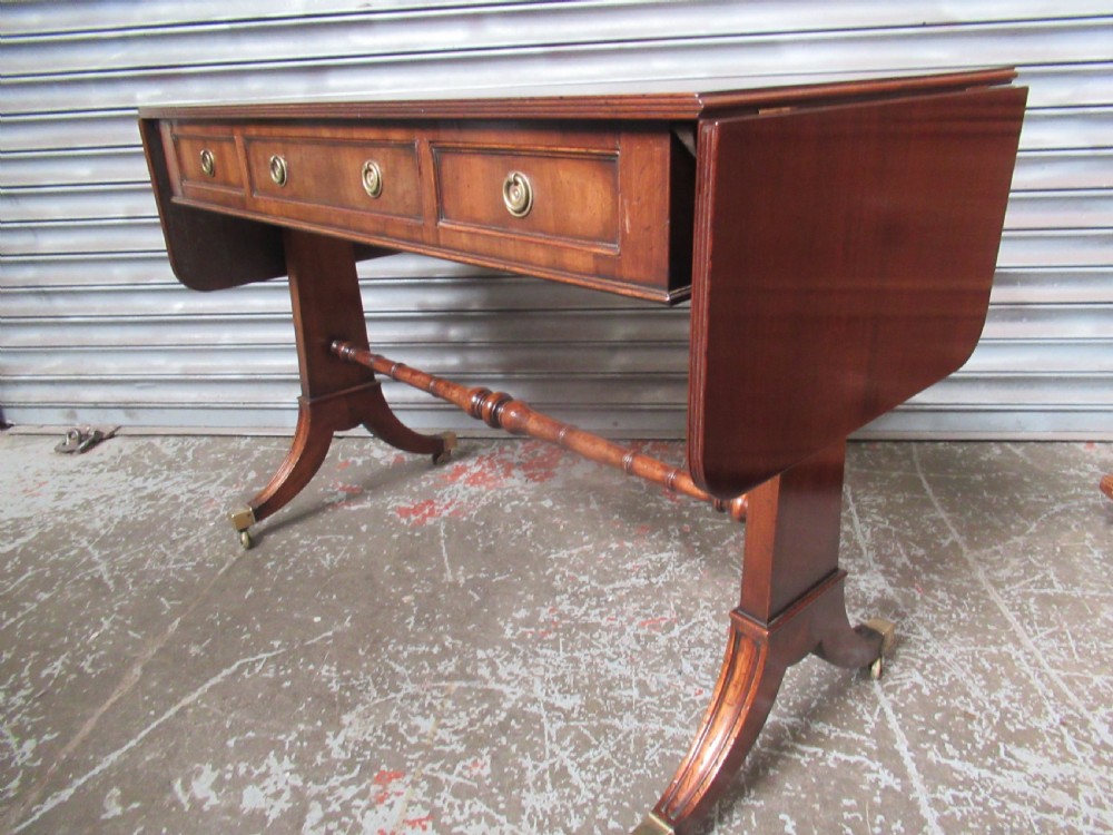 A mahogany sofa table featuring drop-leaf sides, front drawers with brass ring handles, a turned stretcher, and splayed sabre legs with brass castors. View XII