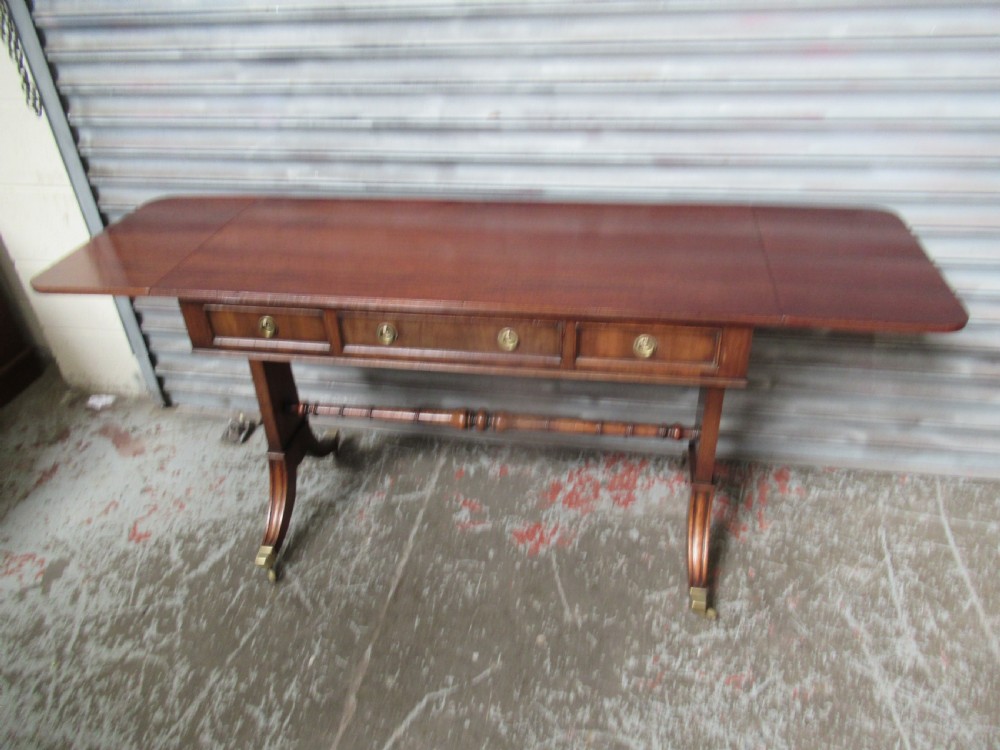 A mahogany sofa table featuring drop-leaf sides, front drawers with brass ring handles, a turned stretcher, and splayed sabre legs with brass castors. View XIII