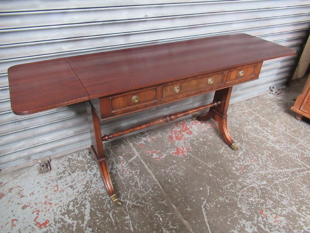 A mahogany sofa table featuring drop-leaf sides, front drawers with brass ring handles, a turned stretcher, and splayed sabre legs with brass castors. View XIV