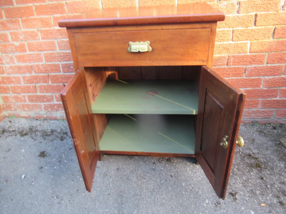 A small warm brown mahogany cupboard featuring a single top drawer with a brass cup handle and two panelled doors below with a brass knob. View VII