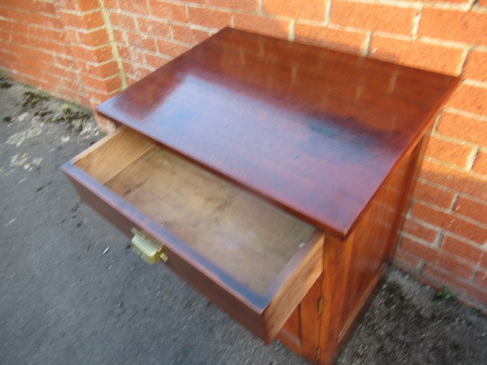 A small warm brown mahogany cupboard featuring a single top drawer with a brass cup handle and two panelled doors below with a brass knob. View X