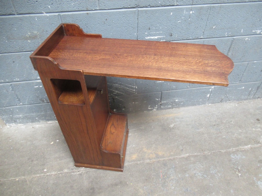 A 1920s warm brown oak magazine rack featuring an integrated cantilevered folding reading table top.