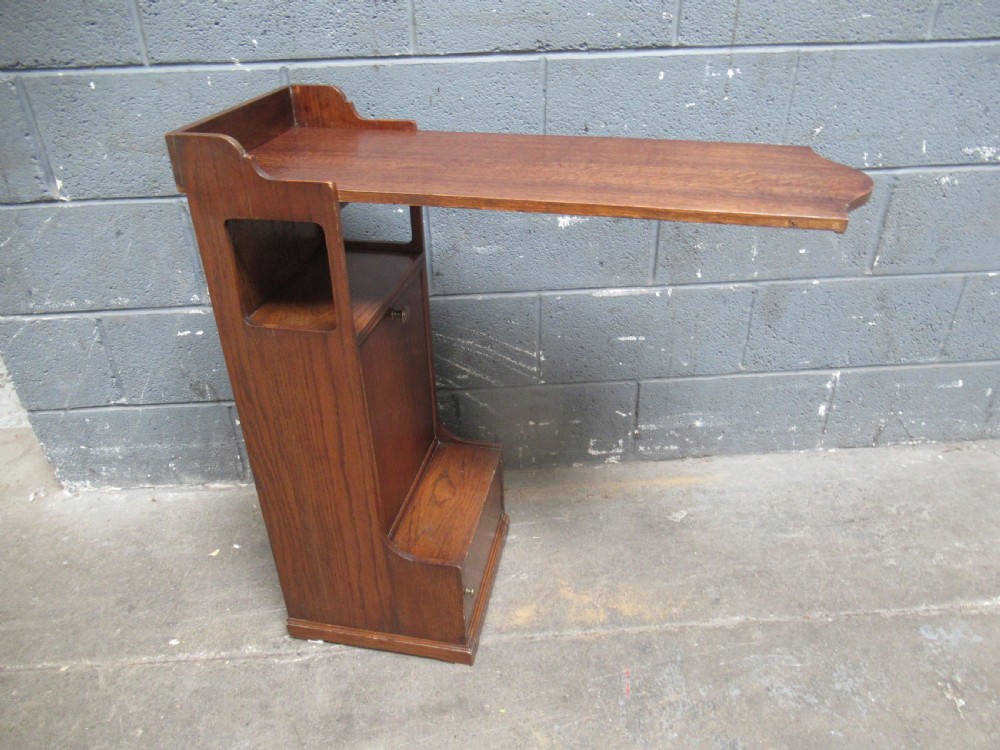 A 1920s warm brown oak magazine rack featuring an integrated cantilevered folding reading table top. View XII