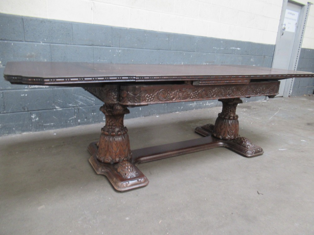 A dark carved oak extending dining table featuring ornate pedestal supports and a carved apron. View III