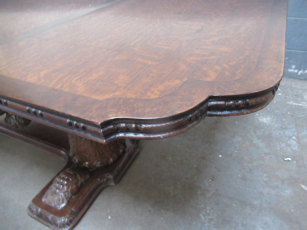 A dark carved oak extending dining table featuring ornate pedestal supports and a carved apron. View IX