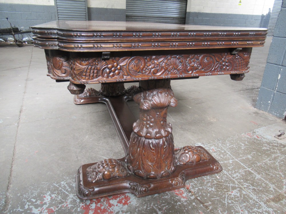 A dark carved oak extending dining table featuring ornate pedestal supports and a carved apron. View XII