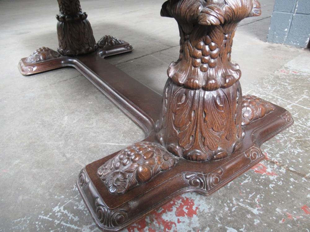 A dark carved oak extending dining table featuring ornate pedestal supports and a carved apron. View XIII