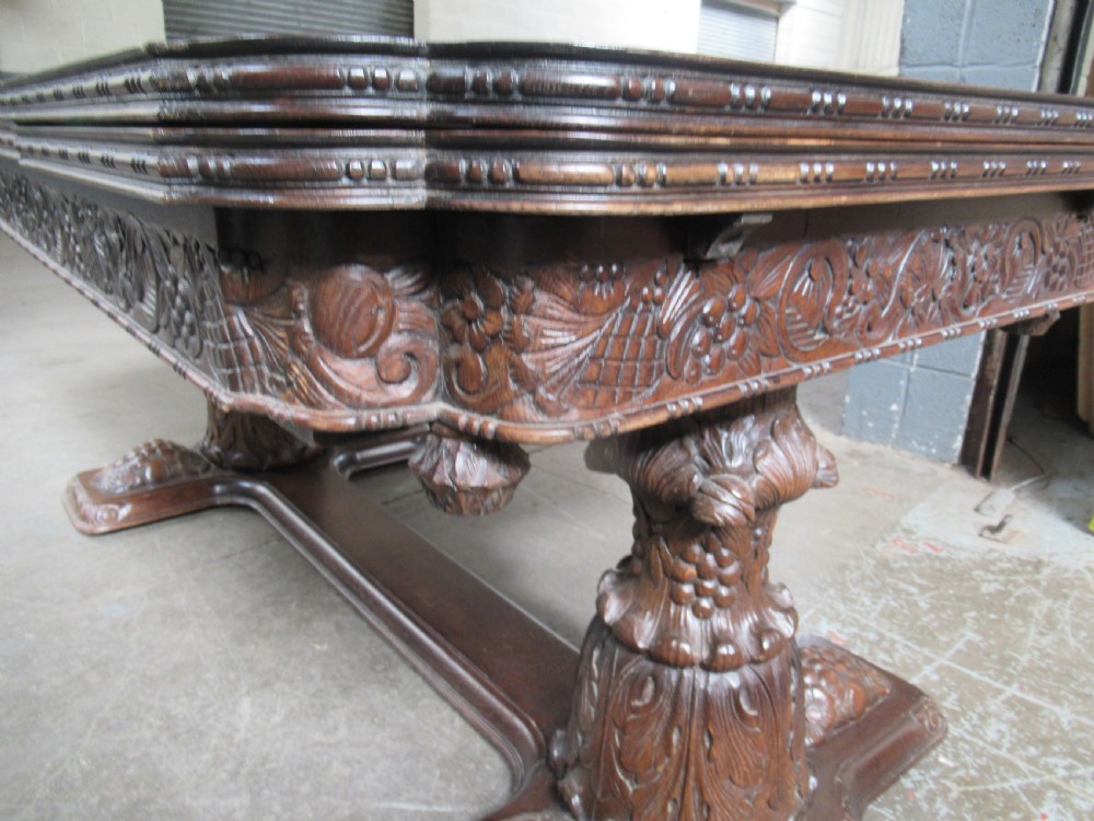A dark carved oak extending dining table featuring ornate pedestal supports and a carved apron. View XIV