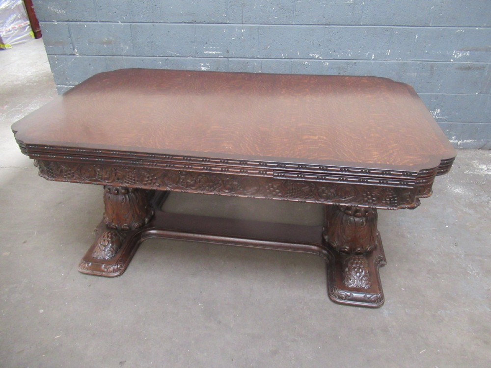 A dark carved oak extending dining table featuring ornate pedestal supports and a carved apron. View XVII