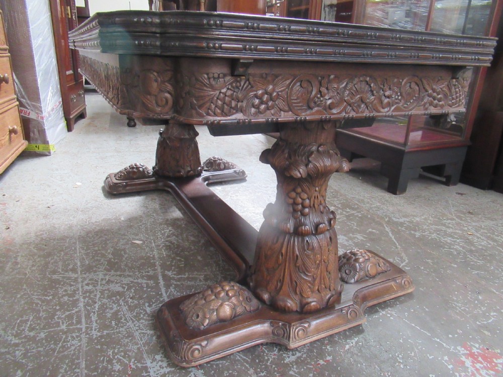 A dark carved oak extending dining table featuring ornate pedestal supports and a carved apron. View XVIII