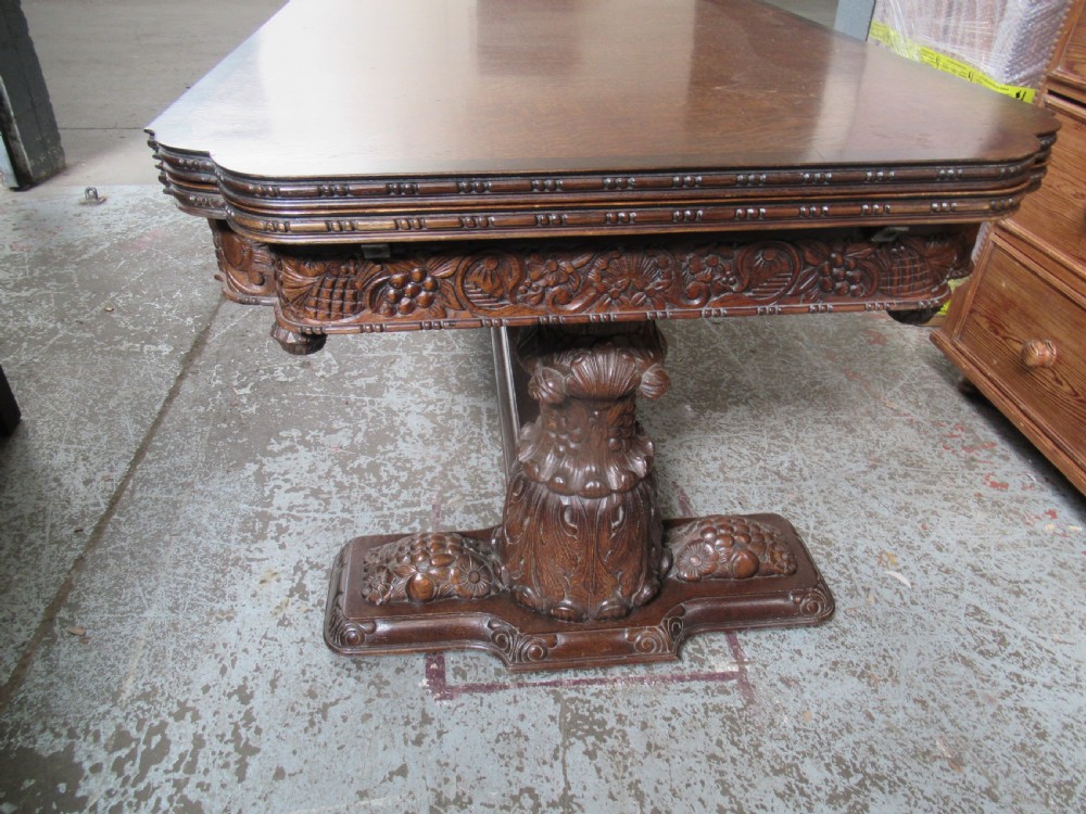 A dark carved oak extending dining table featuring ornate pedestal supports and a carved apron. View XIX