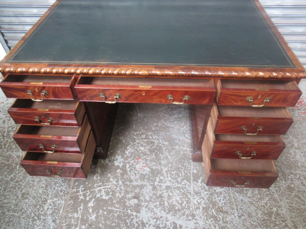 A large mahogany Georgian style pedestal desk featuring a dark green leather writing surface, brass swan-neck handles, and carved rope-twist moulding along the top edge. View XIV