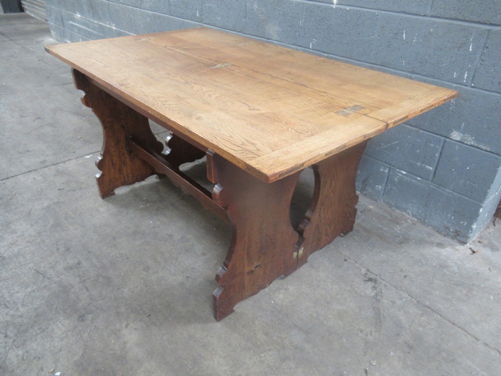 A rectangular 1920s oak fold-over dining table featuring panelled timber top sections, brass hinges, and shaped trestle-style slab supports.
