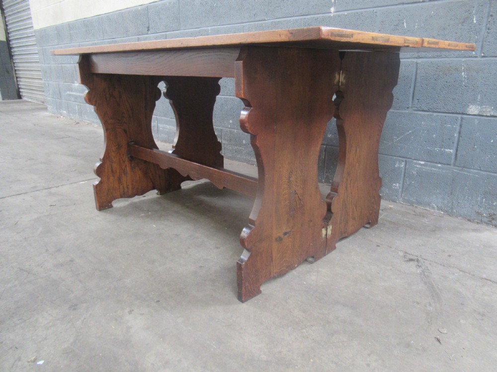 A rectangular 1920s oak fold-over dining table featuring panelled timber top sections, brass hinges, and shaped trestle-style slab supports. View II