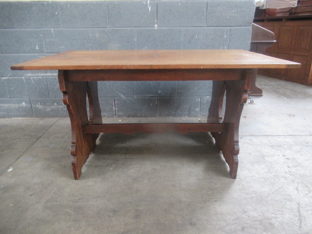 A rectangular 1920s oak fold-over dining table featuring panelled timber top sections, brass hinges, and shaped trestle-style slab supports. View VII