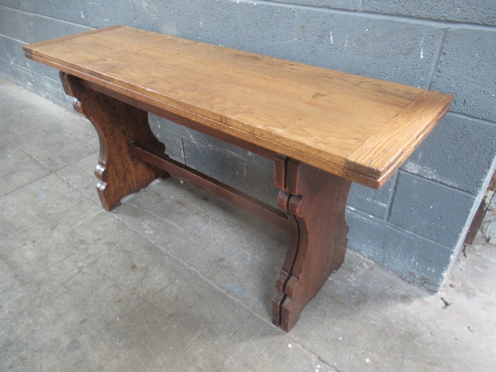 A rectangular 1920s oak fold-over dining table featuring panelled timber top sections, brass hinges, and shaped trestle-style slab supports. View XI