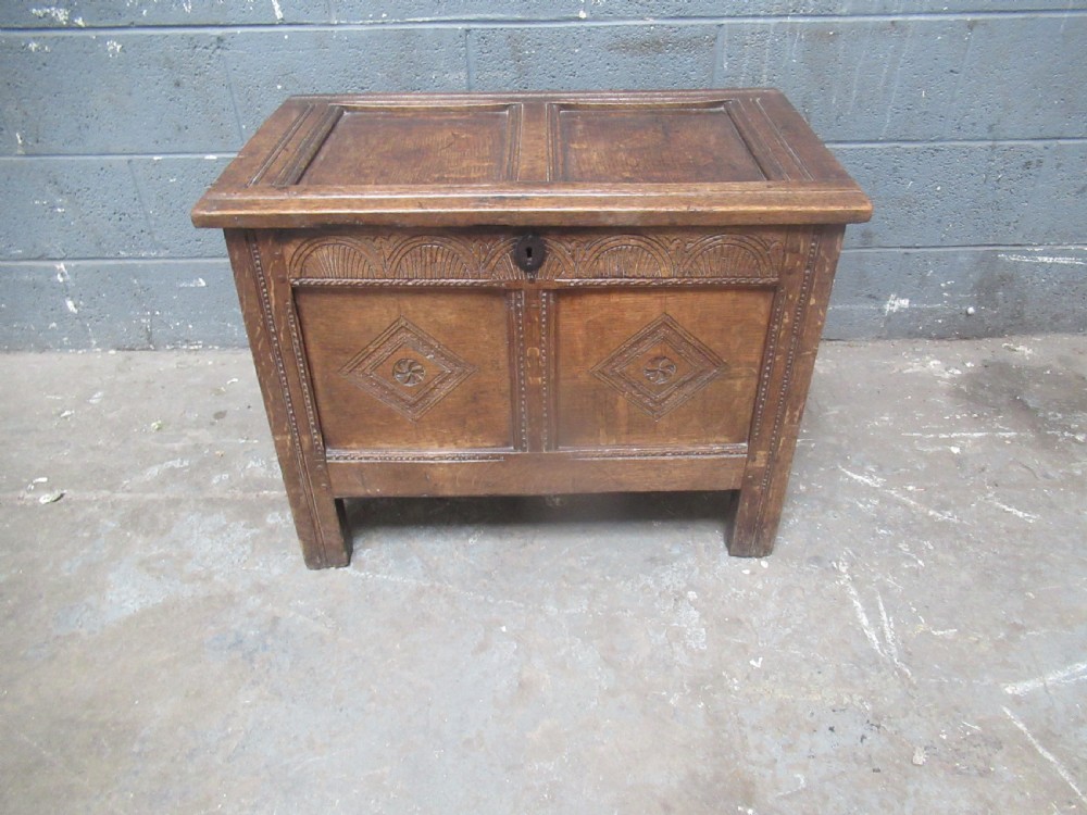 An 18th-century carved oak kist featuring twin front panels with diamond and rosette carvings beneath a lunette-carved top frieze. View II