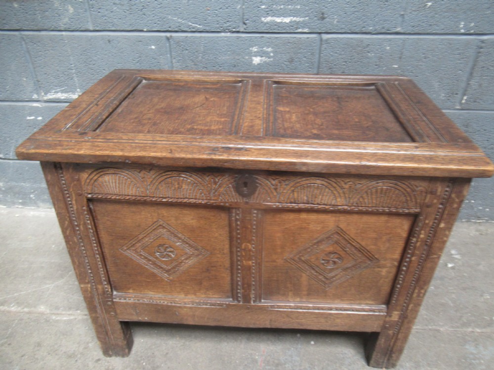 An 18th-century carved oak kist featuring twin front panels with diamond and rosette carvings beneath a lunette-carved top frieze. View IX