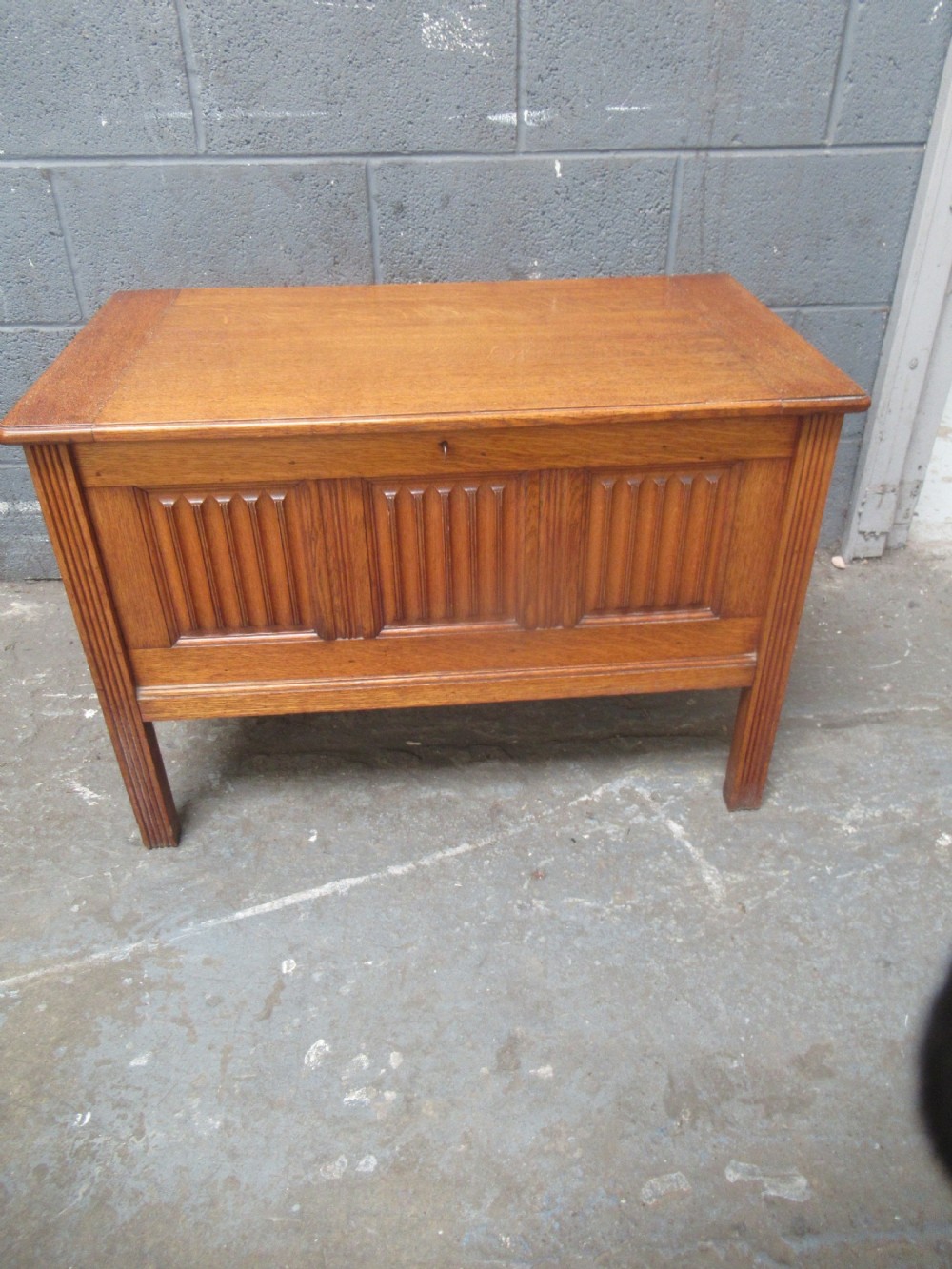 A rectangular light oak blanket box featuring panelled sides, vertical fluted mouldings, and raised block feet.