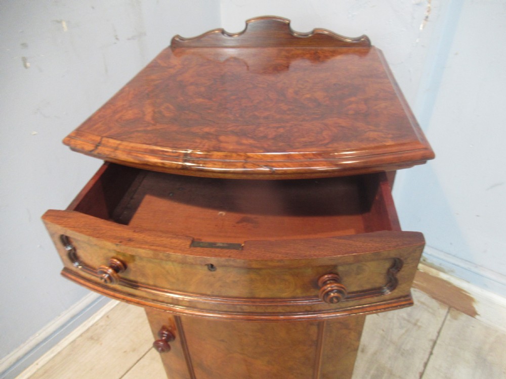 A Victorian burr walnut cabinet featuring a top drawer, a lower cupboard door with a carved shell motif, turned wooden knobs, and a shaped top upstand. View IX
