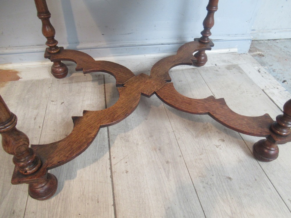An antique warm brown oak side table featuring a single drawer with brass drop handles, a shaped apron, turned legs, and an X-frame stretcher. View VII
