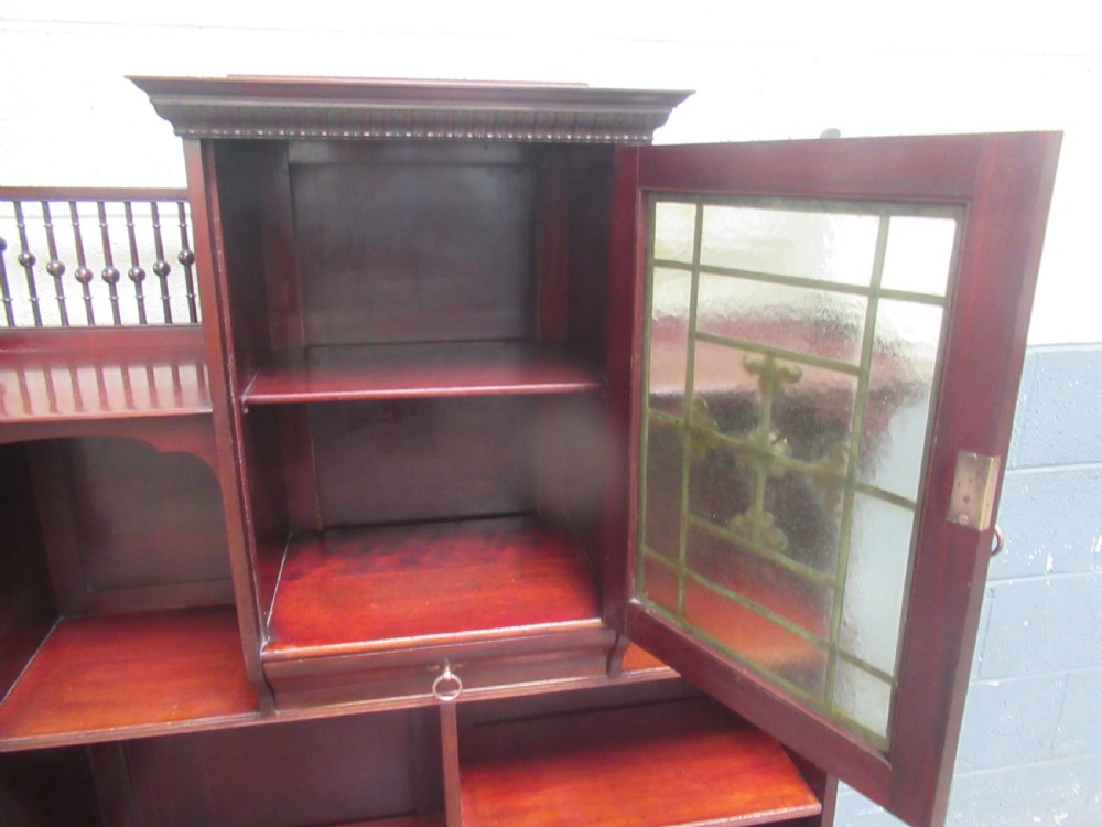 A late Victorian mahogany bookcase featuring a central glazed upper cabinet with decorative metal overlay, flanked by spindle galleries and open shelving below. View VI