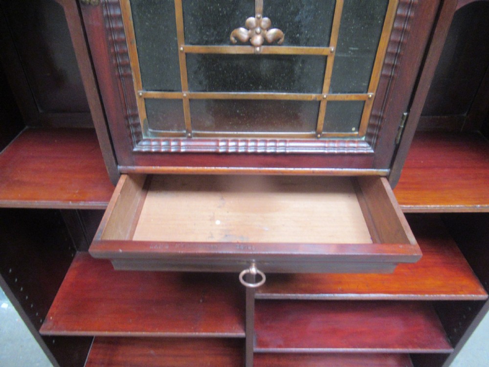 A late Victorian mahogany bookcase featuring a central glazed upper cabinet with decorative metal overlay, flanked by spindle galleries and open shelving below. View IX