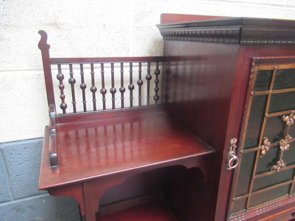 A late Victorian mahogany bookcase featuring a central glazed upper cabinet with decorative metal overlay, flanked by spindle galleries and open shelving below. View XIII