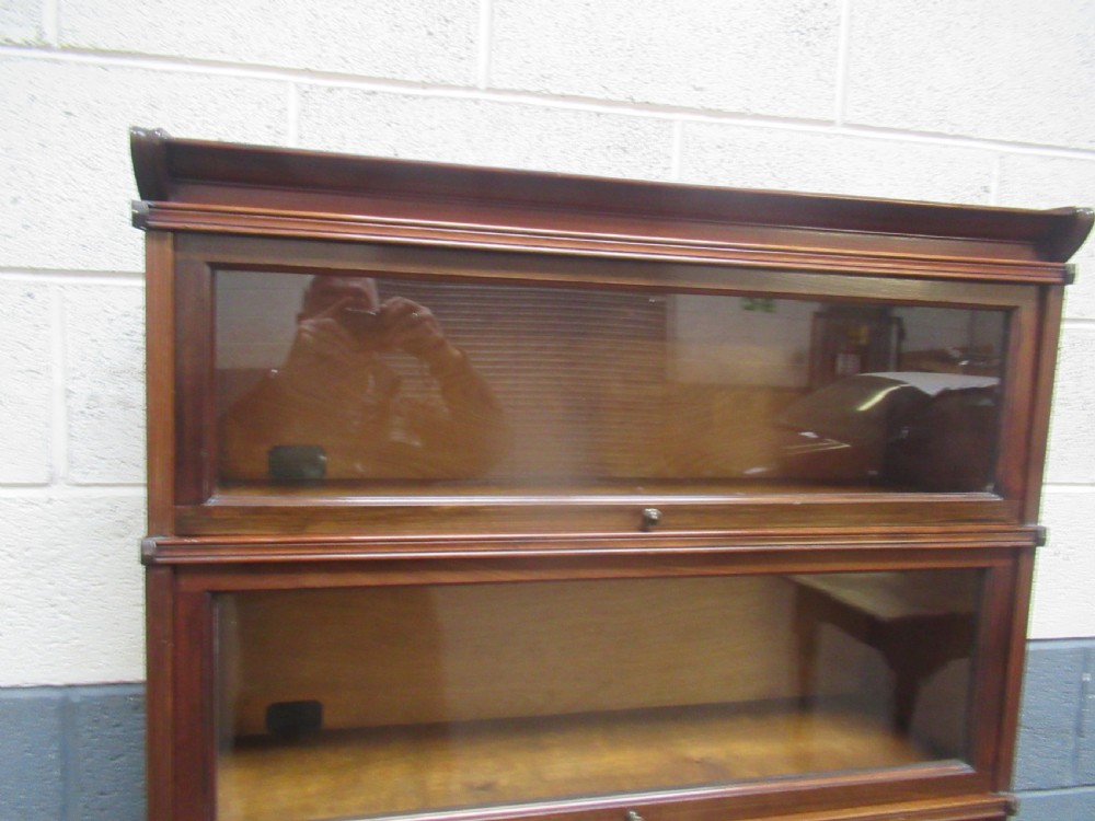 A five-tier mahogany sectional bookcase featuring glazed lift-up doors with small brass knobs and a moulded top cornice. View V
