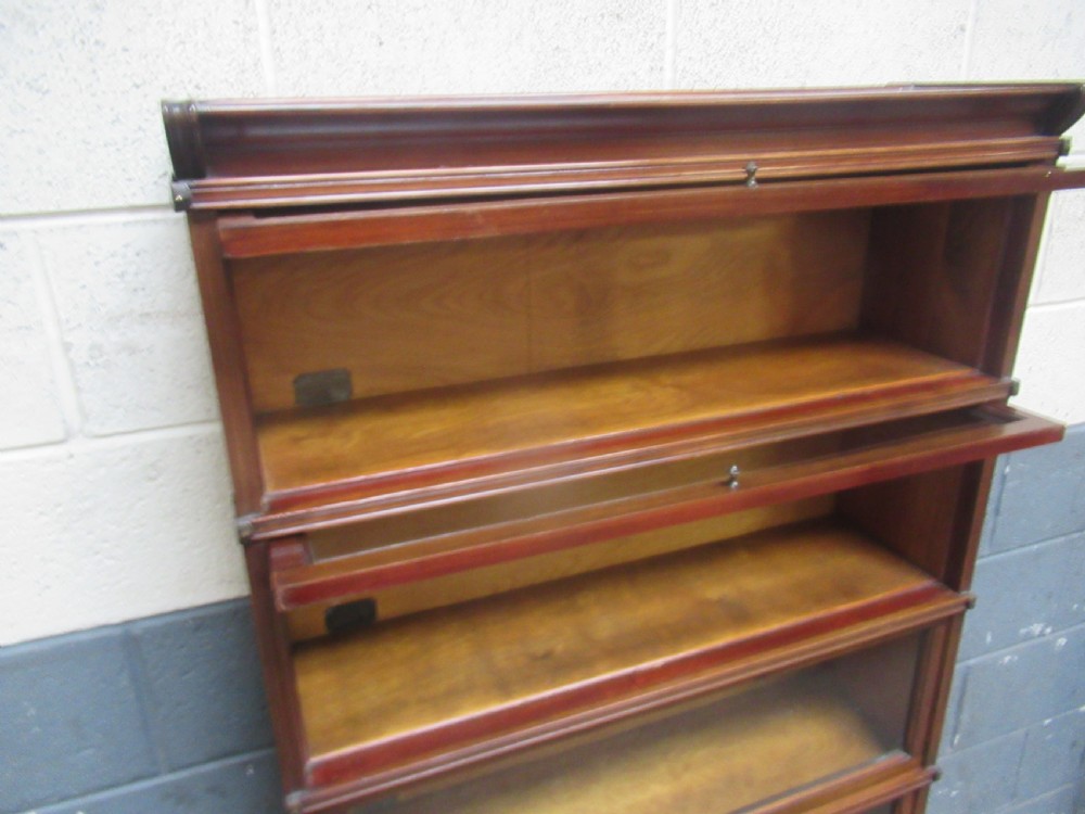 A five-tier mahogany sectional bookcase featuring glazed lift-up doors with small brass knobs and a moulded top cornice. View VII