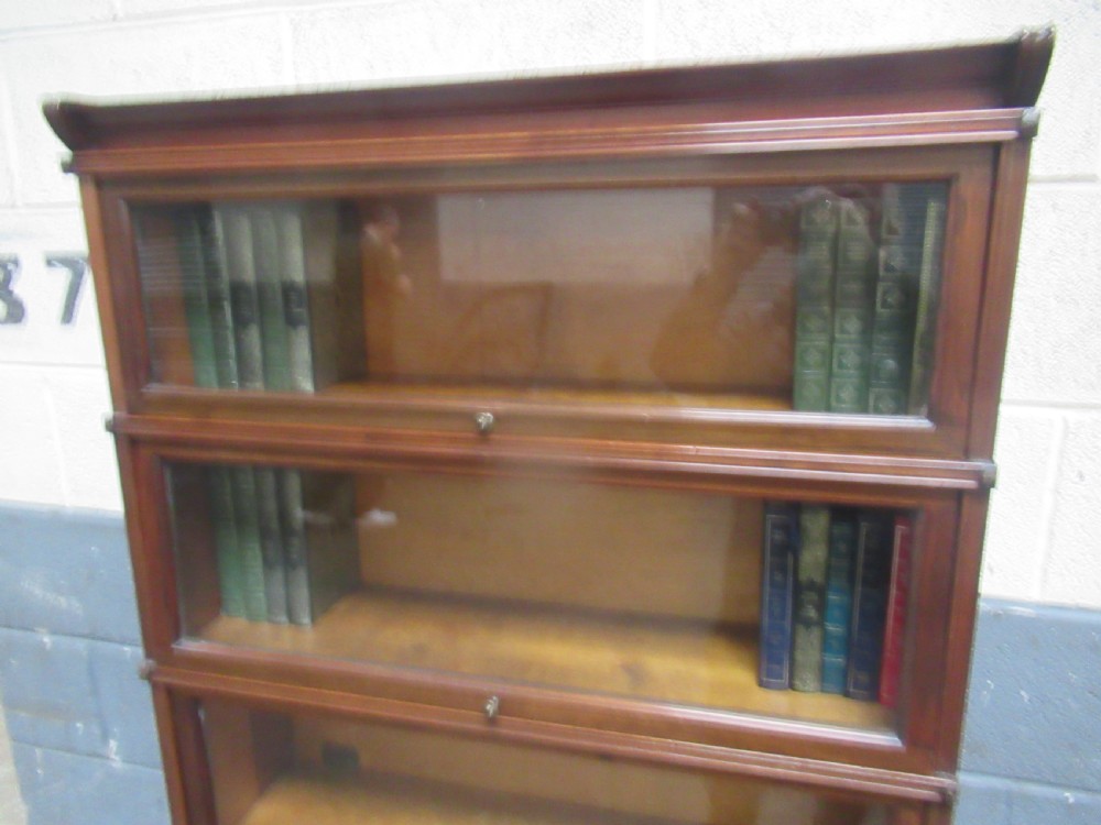A five-tier mahogany sectional bookcase featuring glazed lift-up doors with small brass knobs and a moulded top cornice. View XI