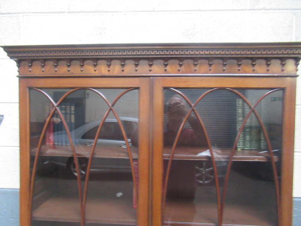 A tall mahogany bookcase featuring two glass upper doors with oval astragal glazing set above two solid lower cupboard doors. View VII