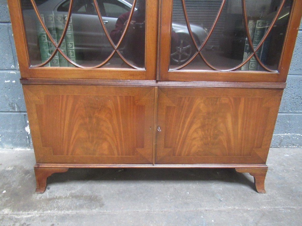 A tall mahogany bookcase featuring two glass upper doors with oval astragal glazing set above two solid lower cupboard doors. View VIII