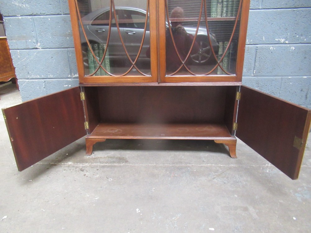 A tall mahogany bookcase featuring two glass upper doors with oval astragal glazing set above two solid lower cupboard doors. View IX