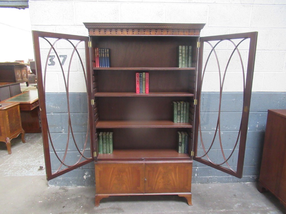 A tall mahogany bookcase featuring two glass upper doors with oval astragal glazing set above two solid lower cupboard doors. View X