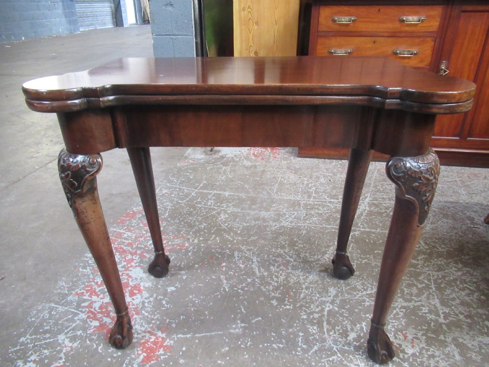 A Georgian mahogany fold-over card table featuring carved cabriole legs with acanthus knees and claw and ball feet.