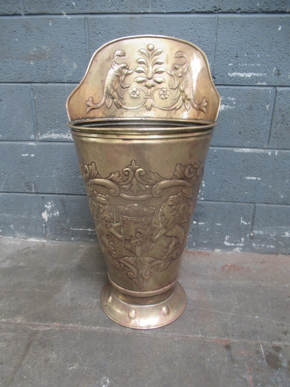 A large embossed brass coal scuttle featuring heraldic lion motifs and a raised back panel.