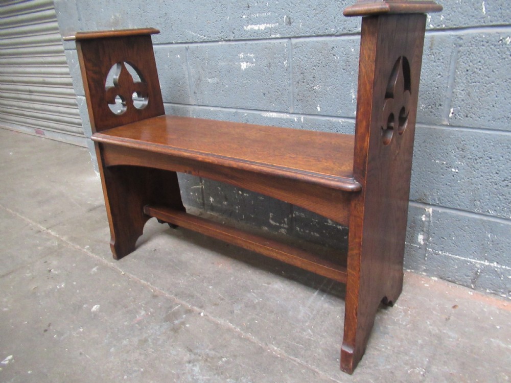 A solid oak Arts and Crafts bench seat with raised side uprights featuring pierced trefoil cutouts.
