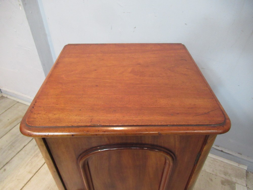 A Victorian mahogany bedside cabinet featuring an arched recessed panel door, a turned wooden knob, and a solid plinth base. View VI