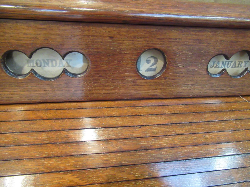 A late Victorian oak stationery cabinet featuring a tambour roll shutter, integrated perpetual calendar at the top, and a lower drawer with brass handle. View III
