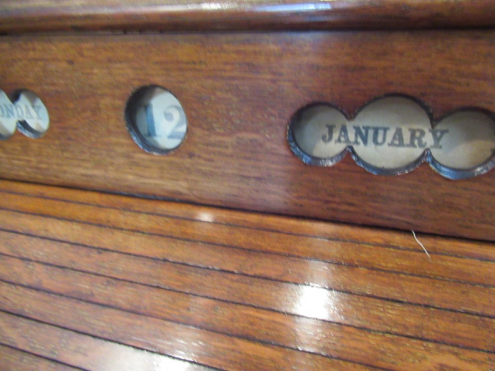A late Victorian oak stationery cabinet featuring a tambour roll shutter, integrated perpetual calendar at the top, and a lower drawer with brass handle. View IV
