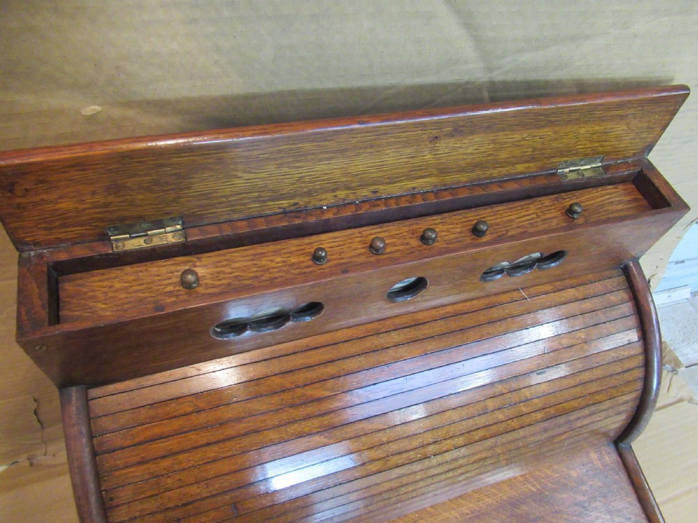 A late Victorian oak stationery cabinet featuring a tambour roll shutter, integrated perpetual calendar at the top, and a lower drawer with brass handle. View V