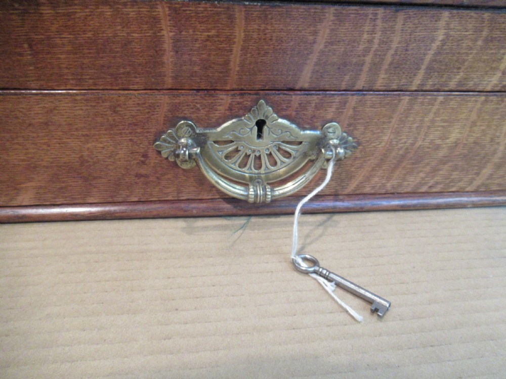 A late Victorian oak stationery cabinet featuring a tambour roll shutter, integrated perpetual calendar at the top, and a lower drawer with brass handle. View VII