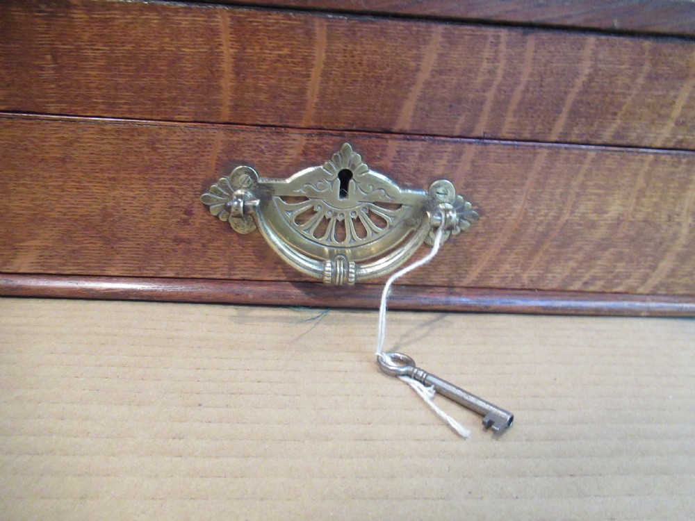 A late Victorian oak stationery cabinet featuring a tambour roll shutter, integrated perpetual calendar at the top, and a lower drawer with brass handle. View VIII
