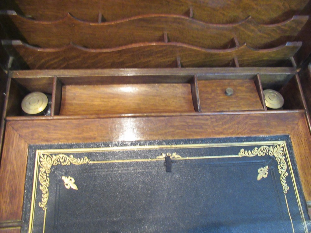A late Victorian oak stationery cabinet featuring a tambour roll shutter, integrated perpetual calendar at the top, and a lower drawer with brass handle. View XII
