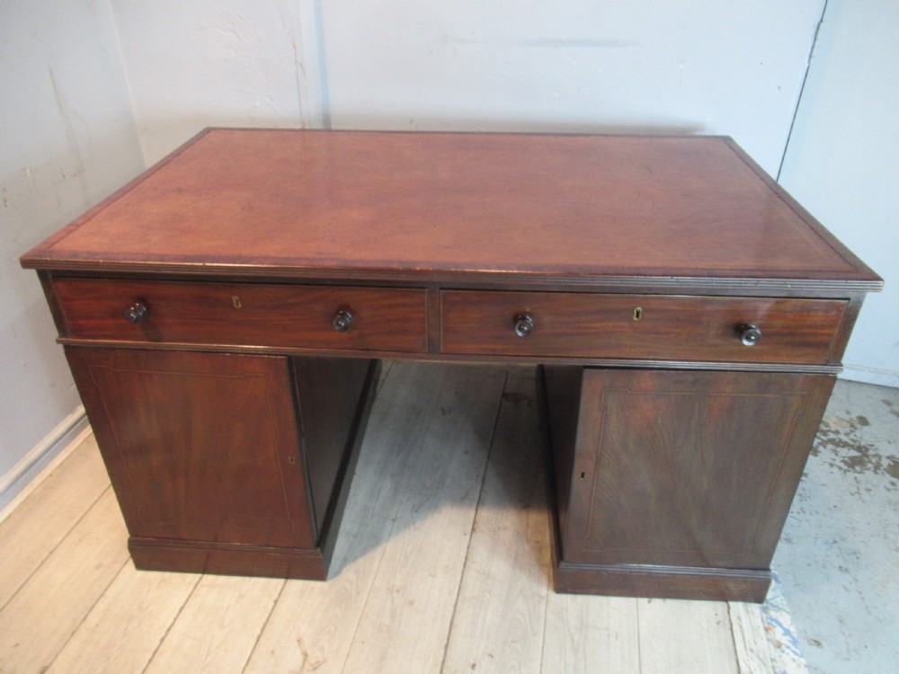 A 19th-century mahogany kneehole desk featuring a leather inset writing surface, two frieze drawers with turned wooden knobs, and two side pedestal cupboards.