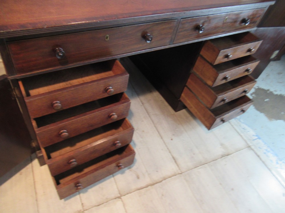 A 19th-century mahogany kneehole desk featuring a leather inset writing surface, two frieze drawers with turned wooden knobs, and two side pedestal cupboards. View XI