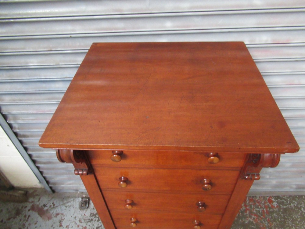 A tall Victorian mahogany Wellington chest featuring seven graduated drawers with turned wooden knobs and carved upper corbels. View V
